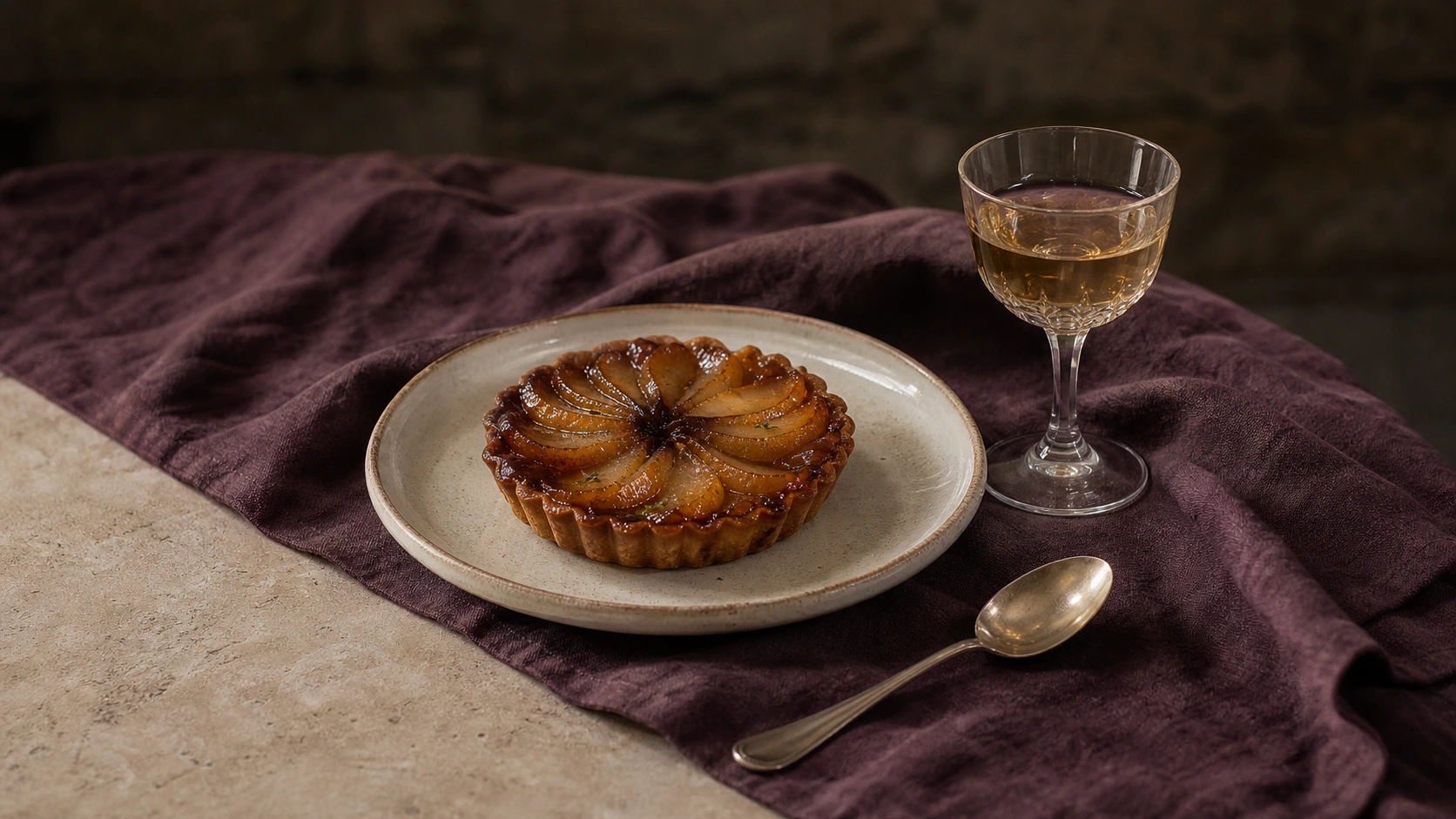 Caramelized pear tart beside a pale amber botanical cordial on plum linen